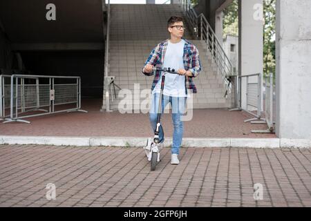 Ein attraktiver Kerl in einem karierten Hemd fährt einen Elektroroller. Stockfoto