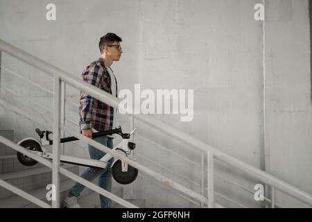 Ein Student steigt mit einem Elektroroller die Treppe zur Universität hinab. Modernes Stadtkonzept. Ökologischer technologischer Lebensstil. Stockfoto