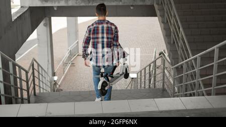 Ein Student steigt mit einem Elektroroller die Treppe zur Universität hinab. Modernes Stadtkonzept. Ökologischer technologischer Lebensstil. Stockfoto