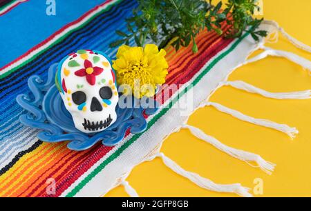 catrina verziert mit gelben Blüten und mexikanischem Poncho auf gelbem Hintergrund. Stockfoto