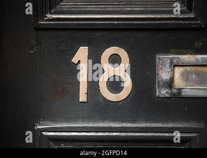 Nummer 18 achtzehn Messingziffern auf glänzend schwarzer Haustür mit Briefkasten sichtbar. Glänzend und sauber. Stockfoto