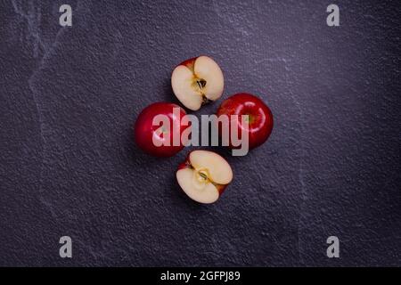 Draufsicht auf geschnittene und ganze rote Äpfel auf einer grauen Oberfläche Stockfoto