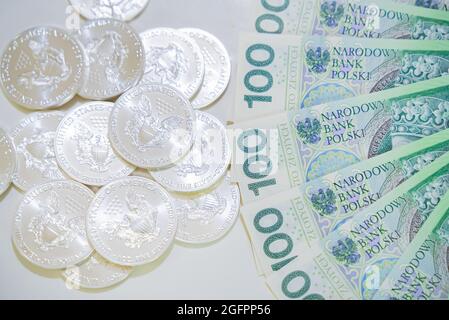 Warschau, Polen 03.05.2021 ein Haufen Münzen daneben spreizte Papiergeld in einem Fächer auf einer weißen Fläche. Hochwertige Fotos Stockfoto