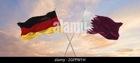 Flaggen von Deutschland und Katar winken im Wind auf Fahnenmasten gegen den Himmel mit Wolken am sonnigen Tag. Symbolisieren Beziehung, Dialog zwischen zwei Ländern Stockfoto