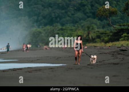 Playa Hermosa, Guanacaste, Costa Rica - 07.26.2020: Eine schöne Frau läuft mit ihrem Hund an der Pazifikküste von Costa Rica Stockfoto