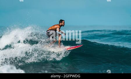 Playa Hermosa, Guanacaste, Costa Rica - 07.26.2020: Ein schönes Profilfoto eines hochqualifizierten Surfers in Shorts, der auf einer großen Welle reitet