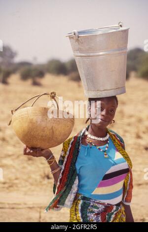 Delaquara, ein Fulani-Dorf, Niger. Junge Frau mit Eimer auf dem Kopf, Kalabash in der Hand. Stockfoto