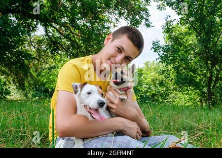 Der Mann umarmt zwei Hunde Jack Russell und einen chihuahua und ruht sich im Park aus Stockfoto