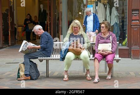 Dort sitzen die Menschen auf einer Bank, jeder auf seine eigene Art und Weise vertieft. Stockfoto