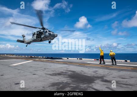 PHILIPPINISCHES MEER (Aug 25, 2021) Aviation Boatswain’s Mate (Handling) 3rd Class Jamari Cooke, rechts, aus Greenville, N.C., zugewiesen an das nach vorne eingesetzte amphibische Angriffsschiff USS America (LHA 6), entdeckt Aviation Boatswain’s Mate (Handling) 3rd Class Ben Rahenkamp, aus Port Maria, Jamaika, ebenfalls in Amerika, Als er einen MH-60S Sea Hawk Hubschrauber vom Hubschrauber Sea Combat Squadron (HSC) 25 zum Start während des Flugbetriebs signalisiert. Amerika und das Luftkampfelement des 31. MEU unterhalten ein strategisches Vordeck für eine Vielzahl von Missionen. Amerika, Flaggschiff der America Expeditionary S Stockfoto