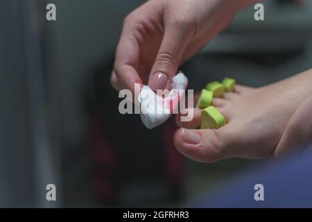 Hand mit Baumwolle und Aceton, um Gel zu entfernen lac auf den Füßen Zehen Nägel Unbekannte Frau, die Pediküre auf ihren Füßen zu Hause Nagellack Entfernen auf dem Fuß Finger Stockfoto