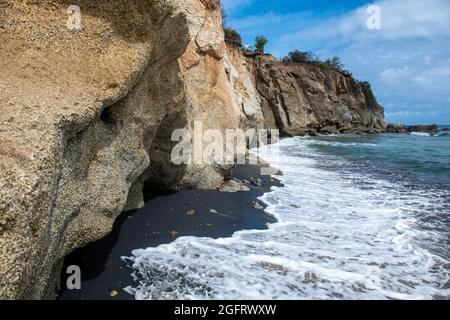 Wasser rauscht über schwarzen Sand unter einer Klippe - Puerto Rico Stockfoto
