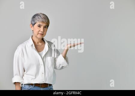 Asiatische Frau mittleren Alters, die auf der Handfläche leeren Platz für Texte oder Produkte auf weißem Hintergrund zeigt Stockfoto