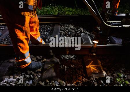 19. August 2021, Baden-Württemberg, Hausach: Ein Mitglied der Baumannschaft löst die Schrauben der Schiene an den Scheren mit einem motorgetriebenen Gerät; in der Mitte des Bildes ist die beschädigte Stelle auf der Schiene zu sehen, die von einer anderen Besatzung markiert wurde. Auch in abgelegenen Regionen des Landes erneuert die Deutsche Bahn ihre Gleissysteme. Eine Baumannschaft aus Offenburg in Baden ist nachts unterwegs und ersetzt die Schienen. (Zur dpa-Sommerserie Baden-Württemberg bei Nacht : ''Machen Sie keinen Fehler' - auf einer nächtlichen Baustelle der Eisenbahn mitten im Schwarzwald') Foto: Philipp von Ditfurth/dp Stockfoto