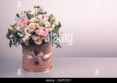 Ein schöner Strauß zarter Blüten aus rosa Rosen, weißen Lilien und gelben Gerberas in einer handgefertigten Schachtel. Alles ist mit grünen palmenlea dekoriert Stockfoto