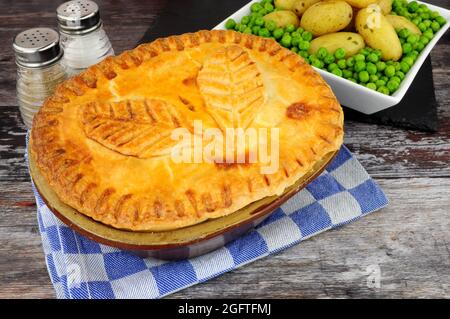 Rindersteak-Pie in einem glasierten Mürbeteiggebäck mit einer Blätterdekoration, serviert mit neuen Kartoffeln und Gartenerbsenbeilage Stockfoto