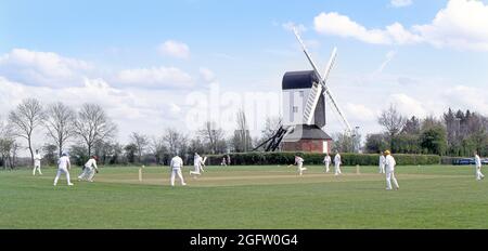 Archiv 1994 Ansicht des späten Frühlings Beginn einer neuen Saison in den 1990er Jahren eines ikonischen Quintessenz englischen Dorf grünen Cricket Spiel mit Bowler Batsman Fielder und Schiedsrichter Spiel vor der idyllischen Windmühle gespielt idyllische Landschaft Landschaft Mountnessing Post Mill in 90er Jahren Archiv Brentwood Essex Countryside England Großbritannien Stockfoto