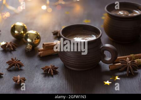 Zwei braune Tonbecher mit schwarzem Kaffee, Weihnachtsdekoration, Gewürze auf dem Holztisch. Selektiver Fokus Stockfoto