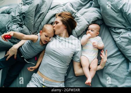 Mama mit Kindern im Schlafanzug auf dem Bett haben Kuscheln und zarte Küsse. Stockfoto