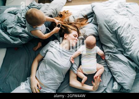 Glückliche, ziemlich langhaarige Mutter genießt es, Zeit mit ihren Kindern zu verbringen. Der jüngste Sohn flechte die Haare der Mutter. Stockfoto