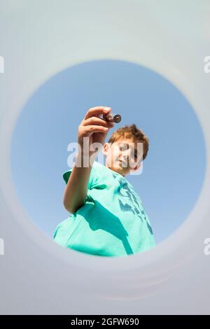 Kind legt einen Stapel in einen Recyclingbehälter, von innen gesehen, mit einem blauen Himmel im Hintergrund. Konzept von Recycling und Bildung in enviro Stockfoto