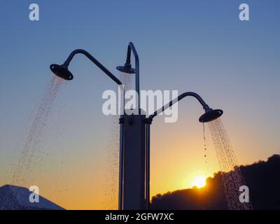 Wasserstrahlen, die aus der dreifachen Stranddusche gegen die untergehende Sonne strömen Stockfoto