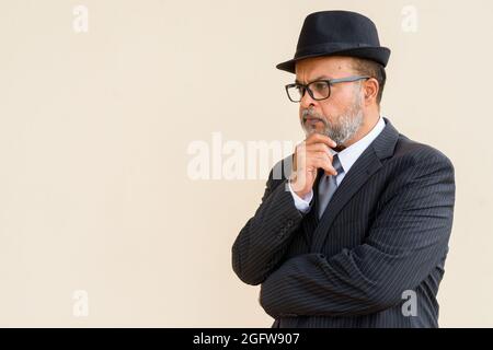 Porträt eines hübschen bärtigen indischen Mannes, der einen Hut an einer einfachen Wand trägt Stockfoto