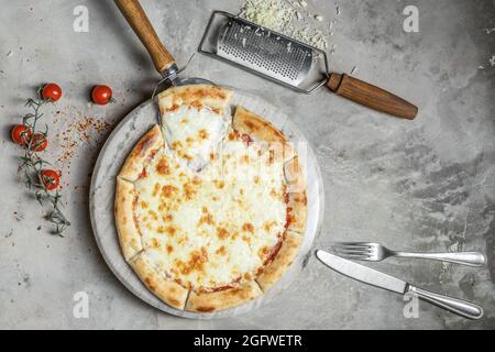Leckere Pizza mit Mozzarella-Käse auf runder Marmorplatte, garniert auf grauem Steinhintergrund mit Pizzazutaten Stockfoto