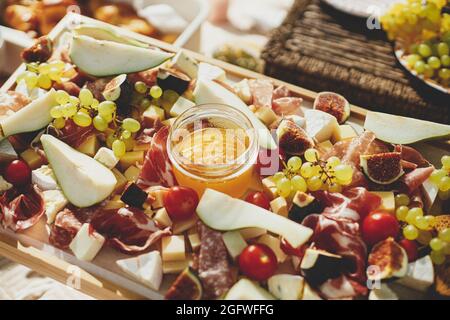 Wurstplatte mit maasdam, Camembert, Brie, Cheddar-Käse und Prosciutto, Salami, Feigen, Honig, Trauben und Kirschtomaten. Antipasti auf Holz, med Stockfoto