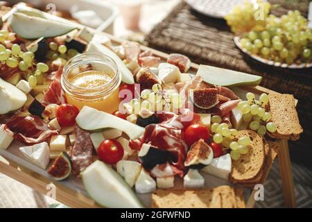 Wurstplatte mit maasdam, Camembert, Brie, Cheddar-Käse und Prosciutto, Salami, Feigen, Honig, Trauben und Kirschtomaten. Antipasti auf Holz, med Stockfoto