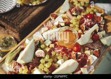 Wurstplatte mit maasdam, Camembert, Brie, Cheddar-Käse und Prosciutto, Salami, Feigen, Honig, Trauben und Kirschtomaten. Antipasti auf Holz, med Stockfoto