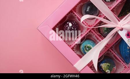Schokoladenbonbons. Rosa Geschenkbox mit handgefertigten Pralinen auf rosa Hintergrund. Festlicher Hintergrund Stockfoto