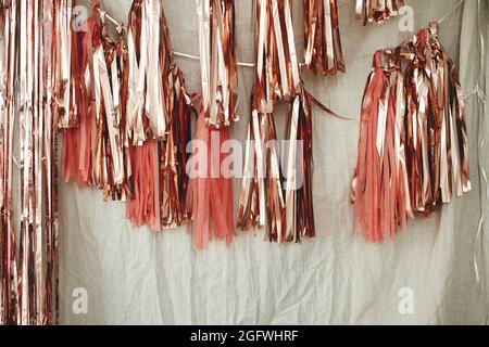 Stilvolle pinke Girlande im Zimmer. Moderne Roségold Quaste Girlande auf beigefarbenem Tuch in modernen Raum für Geburtstagsfeier. Partydekor Stockfoto