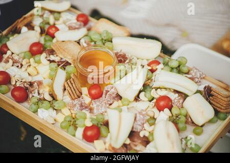 Antipasto. Käseplatte mit maasdam, bree, Cheddar, Prosciutto, Salami, Honig, Trauben, Birnen und Kirschtomaten auf Holz. Charcuterie-Board. Italienisch Stockfoto