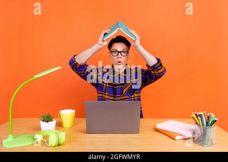 Foto von Millennial beeindruckt Kerl mit Laptop Buch bis tragen karierte Hemd Brille isoliert auf orangefarbenem Hintergrund Stockfoto