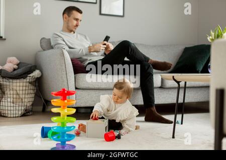 Kleinkind Mädchen spielt im Wohnzimmer, Vater sitzt auf dem Sofa Stockfoto