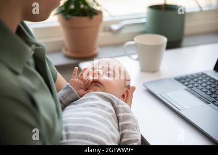 Vater hält einen kleinen Sohn und arbeitet von zu Hause aus Stockfoto