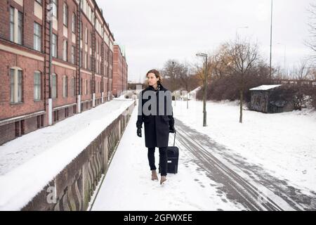 Junger Mann mit Koffer läuft auf verschneiten Gehwegen Stockfoto