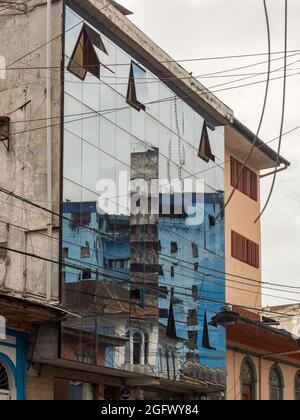 Iquitos, Peru - Dez,2019: Das verlassene, unvollendete, blaue Gebäude spiegelt sich im Glas eines modernen Wolkenkratzers wider. Amazonien, Lateinamerika. Stockfoto