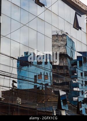 Iquitos, Peru - Dez,2019: Das verlassene, unvollendete, blaue Gebäude spiegelt sich im Glas eines modernen Wolkenkratzers wider. Amazonien, Lateinamerika. Stockfoto