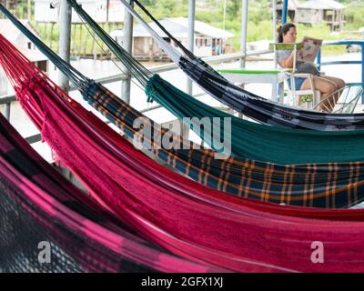 Amazonas, Peru - 12. Dez 2017: Die Frau sitzt hinter schönen, bunten Hängematten auf dem Frachtschiff. Amazonien, Weg von Santa Rosa nach Iquitos. Stockfoto