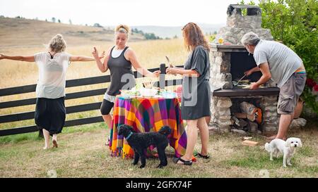 Fröhliche und verspielte Freunde lachen, tanzen und genießen das Bergambiente und grillen vor ihrem Haus Stockfoto