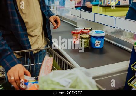 Der Mann legt Lebensmittel aus dem Supermarkt-Korb auf das Förderband. Einkaufen von Lebensmitteln, Kasse im Laden. Stockfoto