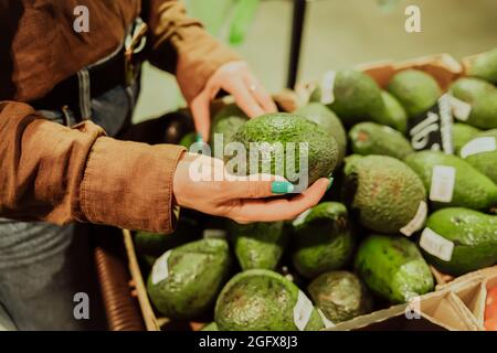 Frau pickt Avocado - grünes Gemüse im Supermarkt oder Markt. Verkauf von gesunden und leckeren Produkt, Vitamine Stockfoto