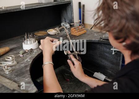 Über der Schulter sehen Sie, wie eine Juwelierin Edelstein mit Handsägen schneidet, während sie Schmuck zum Verkauf anstellt Stockfoto