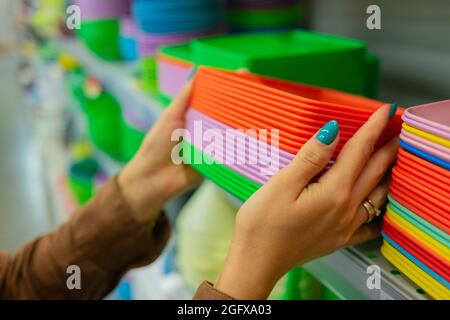 Frau wählt Teller. Einfache Farbauswahl. Regal in einem Laden mit bunten Küchenutensilien Stockfoto