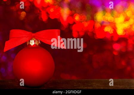 Weihnachtskugel mit roter Schleife vor einem bunt funkelnden Hintergrund, Text- oder Textraum. Stockfoto