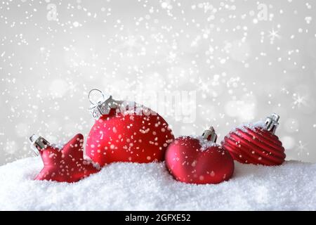 Rote weihnachtskugeln, Stern und Herz auf Schnee, während es schneit, viel Text- oder Textraum. Stockfoto