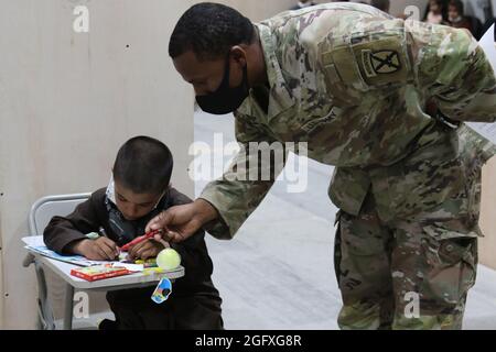 Ein Soldat der US-Armee und ein afghanischer Evakuierungsjunge färben sich im Lager Buehring, Kuwait, am 25. August 2021. Soldaten nahmen an Aktivitäten mit den Kindern Teil, während ihre Familien die Ankunftsverfahren in der Einrichtung durchliefen. (USA Armeefoto von Sgt. Marc Loi) Stockfoto