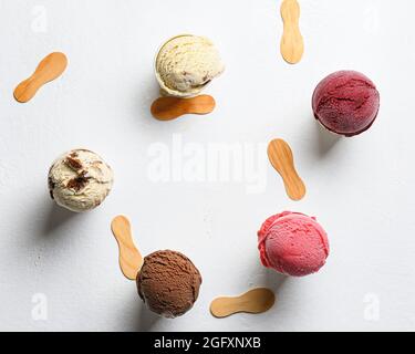 Draufsicht auf Eisschaufeln mit verschiedenen Geschmacksrichtungen auf weißem Hintergrund mit Holzstäben um den Stockfoto